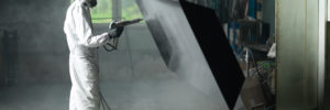 Worker In Protective Gear Sandblasting a Metal Crate